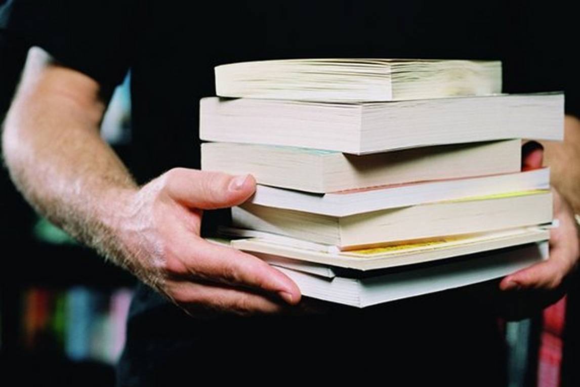 Man holding pile of books with two hands